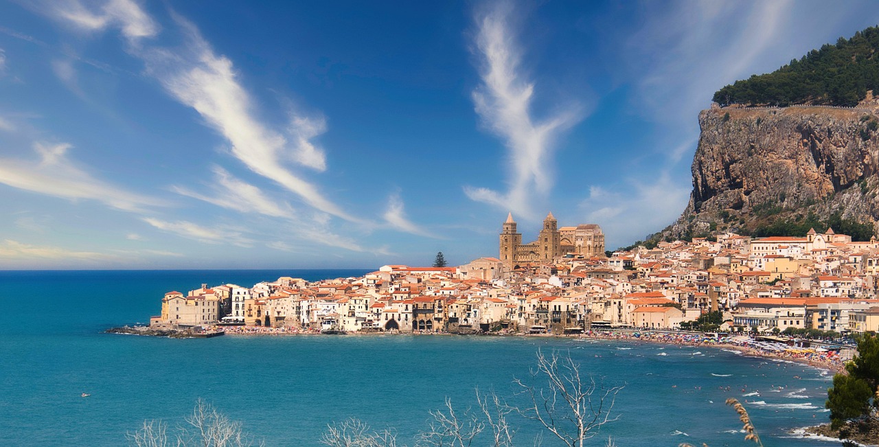Vista panoramica del borgo di Cefalù con mare cristallino e la cattedrale normanna sullo sfondo.